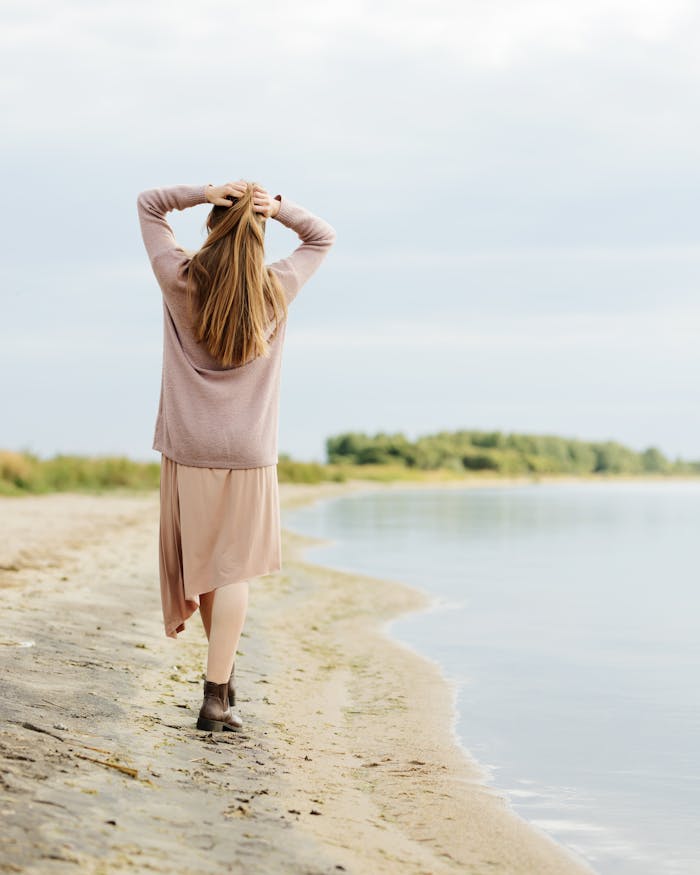 Woman enjoying a peaceful walk on a lakeside beach, embodying relaxation and freedom.